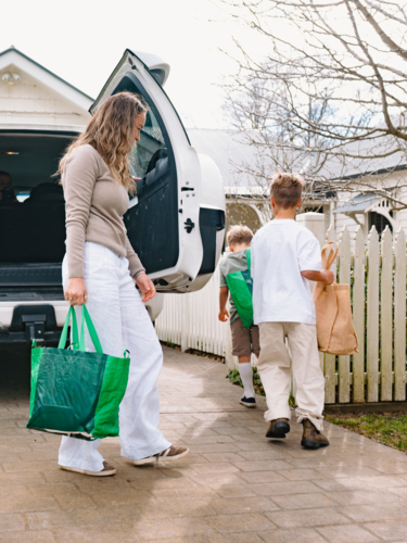 Young boys helping mum carry grocery bags from car boot to the house - Australian Stock Image