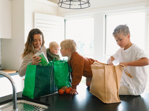 Young boys helping mum take the groceries out of the shopping bag in the countertop - Australian Stock Image