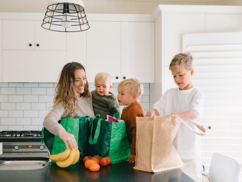 Young boys helping mum take the groceries out of the shopping bag in the countertop - Australian Stock Image