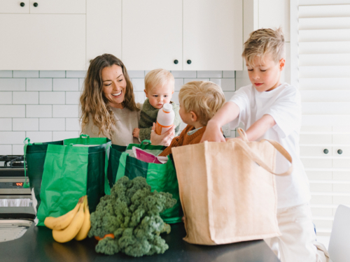 Young boys helping mum take the groceries out of the shopping bag in the countertop - Australian Stock Image