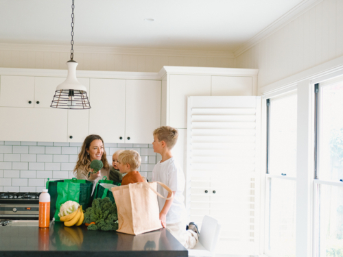 Young boys helping mum take the groceries out of the shopping bag in the countertop - Australian Stock Image