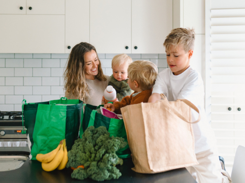 Young boys helping mum take the groceries out of the shopping bag in the countertop - Australian Stock Image
