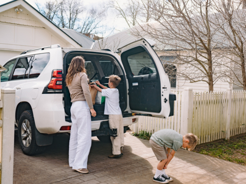 Young boys helping mum unload grocery bags from car boot - Australian Stock Image