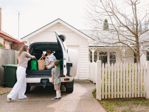 Young boys helping mum unload grocery bags from car boot - Australian Stock Image