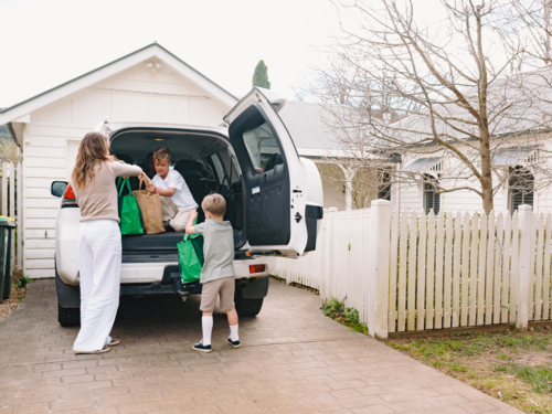 Young boys helping mum unload grocery bags from car boot - Australian Stock Image