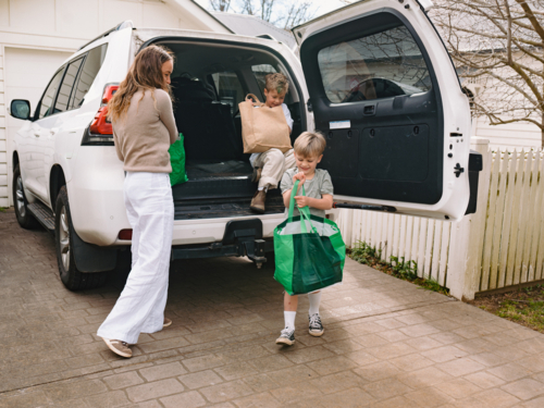 Young boys helping mum unload grocery bags from car boot - Australian Stock Image