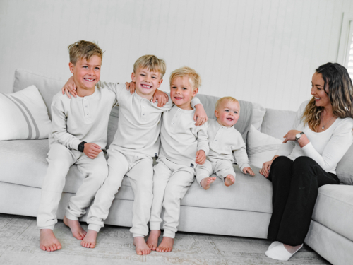 Young boys in their pajamas sitting on the couch arms-in-arms with mum on the side - Australian Stock Image