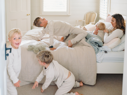 Young boys play and tumble around mum lying on the bed - Australian Stock Image