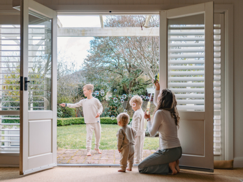 Young boys playing in the patio with mum kneeling by the doorway - Australian Stock Image