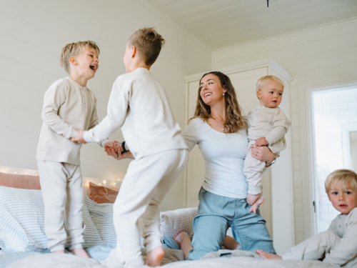 Young boys playing on the bed jumping with mum holding baby brother - Australian Stock Image