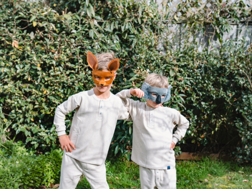 Young boys wearing animal masks standing in front green foliage - Australian Stock Image
