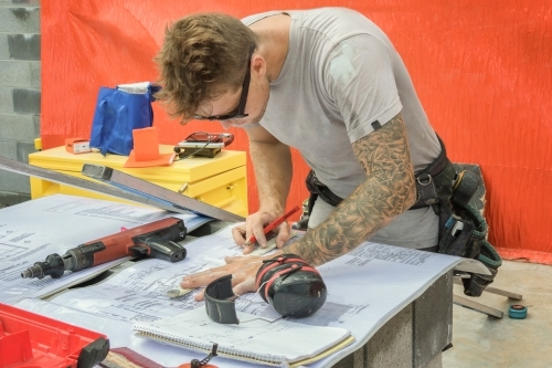 Young builder checking plans on residential construction site - Australian Stock Image