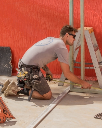 Young builder using tape measure on residential construction site - Australian Stock Image