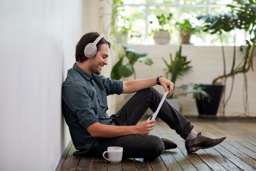 Young business man sitting, reading on a timber studio floor - Australian Stock Image