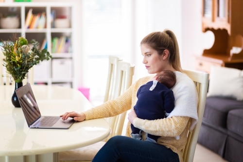 Young businesswoman mum working from home on laptop with newborn baby - Australian Stock Image