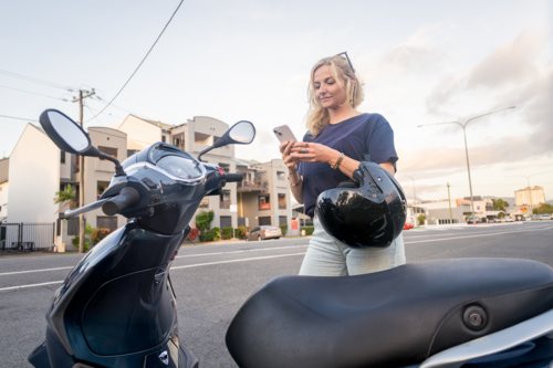 Young Caucasian woman checking her phone before riding her scooter - Australian Stock Image