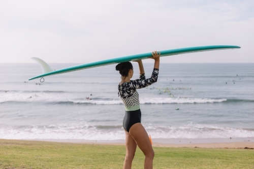 Young caucasian women holding longboard surfboard while looking at the waves