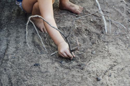 Young child playing with sticks in sandy grey dirt