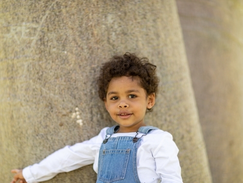 young child standing near big tree trunks - Australian Stock Image