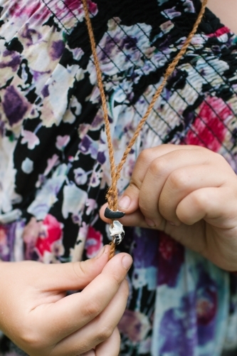 Young child wearing a woven necklace while holding a shell pendant. - Australian Stock Image