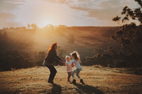Young children playing with their mother in a field at sunset - Australian Stock Image
