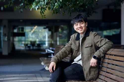Young Chinese man smiling whilst listening to wireless headphones - Australian Stock Image