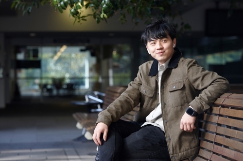 Young Chinese man smiling whilst listening to wireless headphones - Australian Stock Image