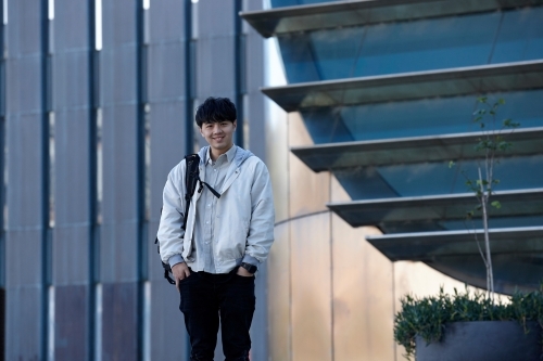 Young Chinese man smiling with backpack at university campus - Australian Stock Image
