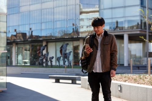 Young Chinese student outdoors checking mobile phone - Australian Stock Image