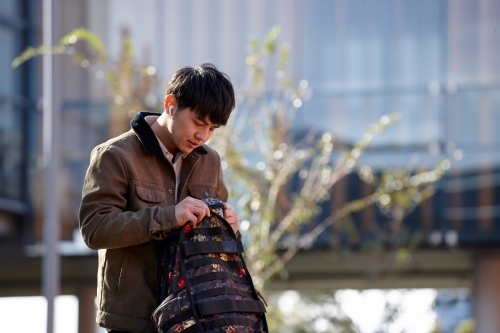 Young Chinese student outdoors opening backpack - Australian Stock Image