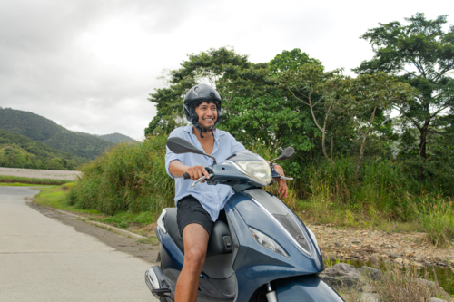 Young Cook Islander man riding a motorbike alone on a rural road in Far North Queensland - Australian Stock Image