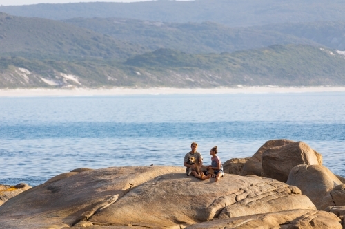 young couple and dog sitting on granite rock by the sea - Australian Stock Image