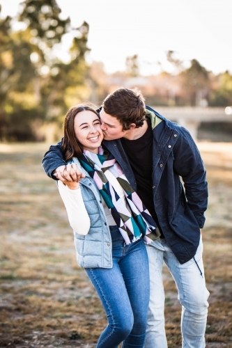 Young couple holding hands walking while man kisses woman on cheek