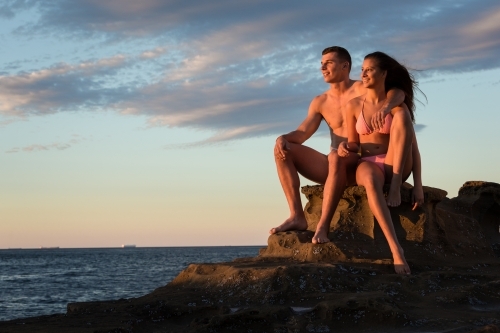 Young couple on the ocean rocks at sunrise