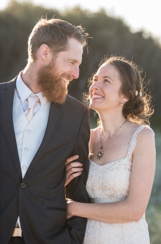 Young couple on wedding day strolling along outdoors in portrait mode. - Australian Stock Image