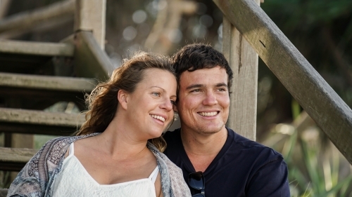 Young couple sitting on beach steps looking at ocean - Australian Stock Image