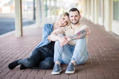Young couple sitting on brick pathway with woman's head resting on man's shoulder - Australian Stock Image