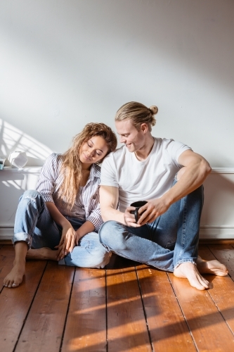 Young couple sitting on the floor relaxing at home - Australian Stock Image