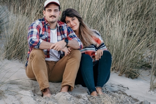 Young couple sitting on the sand at the beach. - Australian Stock Image