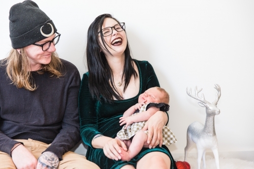 Young couple sitting together mum holding newborn baby head thrown back laughing