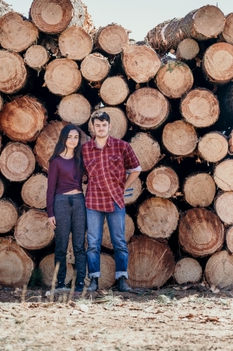 Young couple stand in front of timber pile.