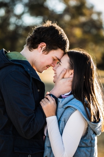 Young couple standing close together foreheads touching him touching her face smiling - Australian Stock Image