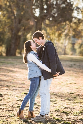 Young couple standing close together holding hands looking at each other smiling - Australian Stock Image