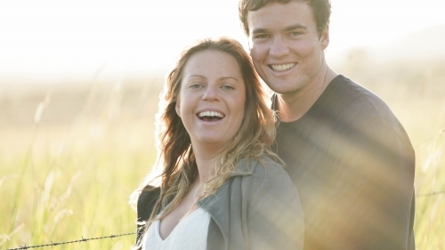 Young couple standing in field, looking at camera, sun flare behind