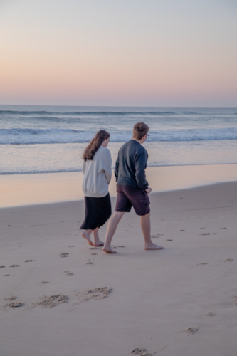 Young couple walking along the beach at sunrise - Australian Stock Image