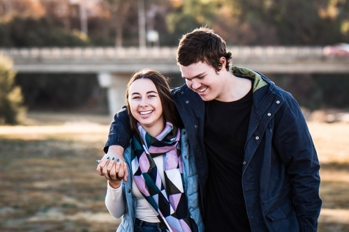 Young couple walking in park holding hands and smiling - Australian Stock Image