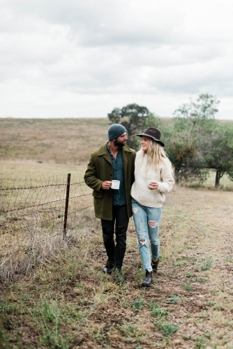 Young couple walking through farm holding cups of coffee - Australian Stock Image