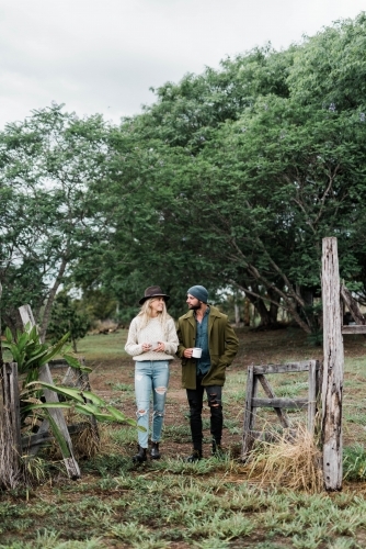 Young couple walking through farm holding cups of coffee - Australian Stock Image