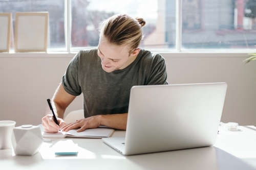 Young creative guy with blond bun making notes in a studio - Australian Stock Image