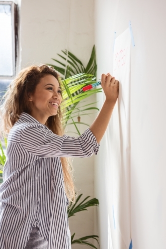 Young creative woman writing on butchers paper during a planning session - Australian Stock Image